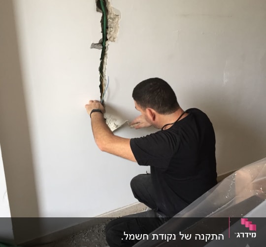 חשמלאי עובד על חוטים בקיר פתוח